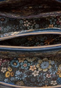 Innenseite einer Brieftasche mit floralem Muster, drei Fächern, dunklem Hintergrund mit bunten Blumen, goldenen Reißverschlüssen und strukturiertem Futter.