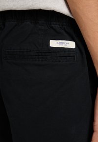 Zwarte stoffen broek met een achterzak en een genaaide label "ELEMENT CO. SINCE 1992," en een elastische tailleband voor comfort.