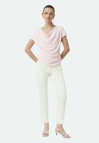 Gepersonaliseerde roze top met een brede halslijn, gecombineerd met witte aansluitende broek en witte bandjeshakken. Gladde stoftextuur en op maat gemaakte pasvorm.