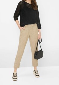 Pull noir en maille ouverte, pantalon en lin beige avec ceinture élastique, sac à main tissé noir, et sneakers élégants noir et crème.