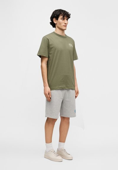 Πράσινο ελιάς βαμβακερό μπλουζάκι με στρογγυλή λαιμόκοψη, σετ με γκρι βαμβακερά σορτς και μπεζ αθλητικά παπούτσια, με διακριτικό λογότυπο στο στήθος.