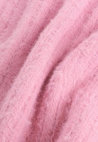 Tissu tricoté rose doux avec une texture duveteuse, montrant des brins de fibre détaillés et des plis subtils créant des ombres et de la profondeur.