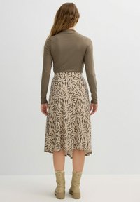 Top de manga larga en color oliva combinado con una falda beige con un patrón floral. Longitud hasta la rodilla con una silueta fluida, complementada con botas marrón claro.