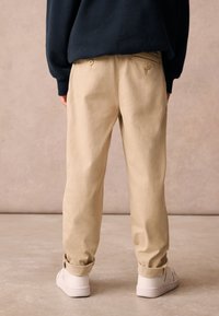 Chinos beige con una vestibilità comoda, dotati di una cintura con bottoni e risvolti, abbinati a sneaker bianche. Tessuto di cotone liscio.