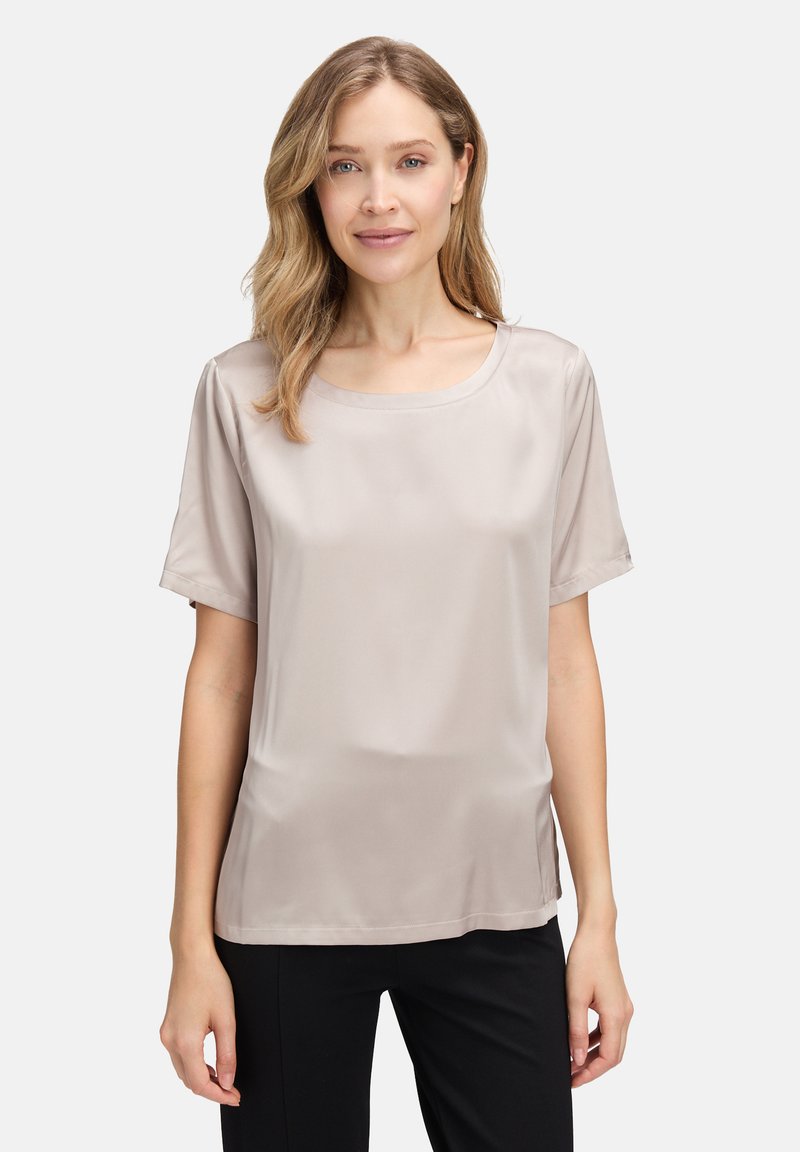 Lichtbeige satijnen blouse met een ronde halslijn en korte mouwen. Gebogen zoom en zachte textuur, gecombineerd met zwarte broeken.