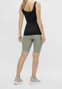 Svart linne och olivgröna cykelshorts med en tight passform. Sneakers har ljusgrå och korallfärgade detaljer. Bakifrån visad vy.