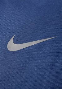 Tissu bleu avec un tissage texturé mettant en avant un logo Swoosh Nike argenté. Le matériau semble durable et lisse.