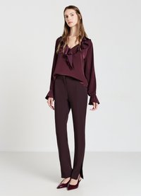 Blusa in raso bordeaux con scollatura arricciata, abbinata a pantaloni sartoriali bordeaux con spacchi laterali e décolleté appuntite abbinate.