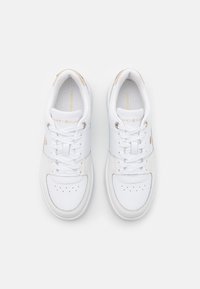 Białe trampki wykonane z materiałów skórzanych i siateczkowych, o okrągłym nosie, teksturowanych detalach oraz kontrastowym złotym logo na języku i boku.