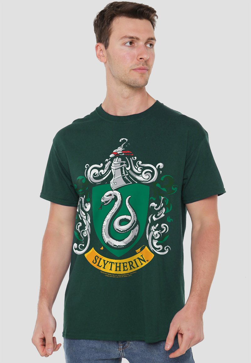 Young man wearing dark green Slytherin crest t-shirt with a coiled silver snake and decorative helmet design, looking to the side.