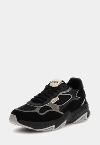 Baskets de sport noires composées d'un mélange de matériaux, incluant du mesh et du daim, avec des accents noirs et gris, et un design de semelle épaisse.