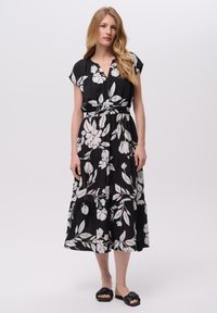 Czarna maxi sukienka w biały kwiatowy wzór, z krótkimi rękawami, dekoltem w kształcie litery V i paskiem w talii. Lekki materiał ma warstwowy fason.
