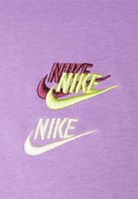Lila tyg med tre broderade Nike-logotyper. Den översta logotypen är mörkröd, den mellersta neongrön och den nedersta vit med en gul accent.