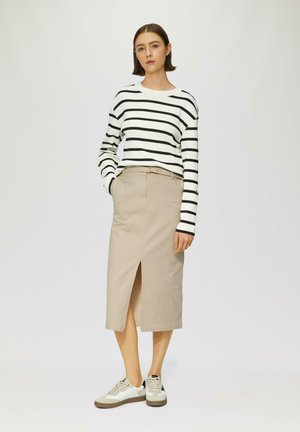 Chemise à rayures noir et blanc à manches longues associée à une jupe beige avec une fente à l'avant, complétée par des baskets légères avec des accents beige.