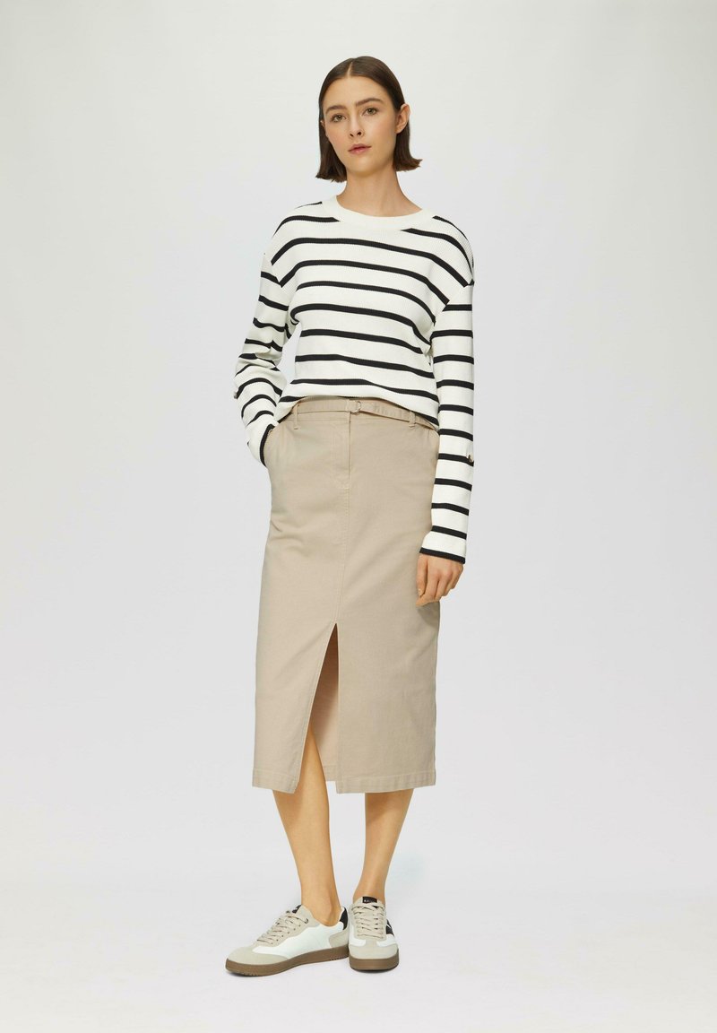 Chemise à rayures noir et blanc à manches longues associée à une jupe beige avec une fente à l'avant, complétée par des baskets légères avec des accents beige.