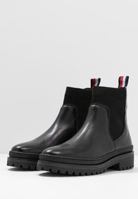 Mustat nahkaiset Chelsea-saappaat, joissa on joustavat sivupaneelit, teksturoitu pinta, kontrastiväri musta paksu pohja sekä monivärinen vetonauha takana.