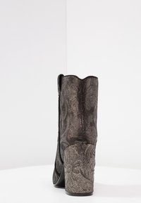 Černá metalická kotníková bota s texturačním květinovým vzorem, vlnitým horním okrajem a masivním podpatkem, která vyniká hladkým povrchem a elegantním designem.