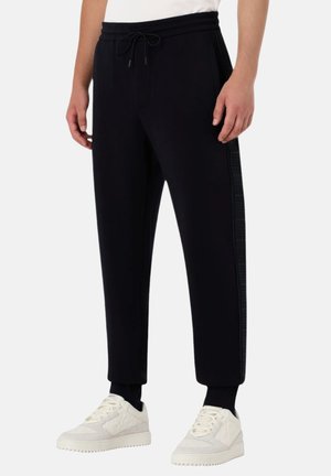 Sorte joggerbukser med elastisk talje, snor, ribbede manchetter og teksturerede sidestriber. Båret med hvide sneakers.