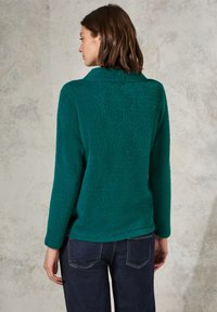 Türkisfarbener Fleece-Pullover mit lockerer Passform, hohem Kragen und langen Ärmeln. Weiche Textur mit abgerundetem Saum und seitlichen Schlitzen.