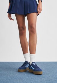 Blå semsket plattform-sneakers med lyseblå striper, med en strukturert gummisåle. Brukt med hvite ribbestrikkede ankelsokker.