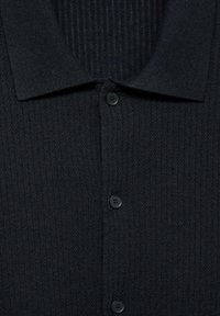 Cardigan nero a coste con colletto strutturato, presenta tre bottoni neri e una finitura testurizzata.