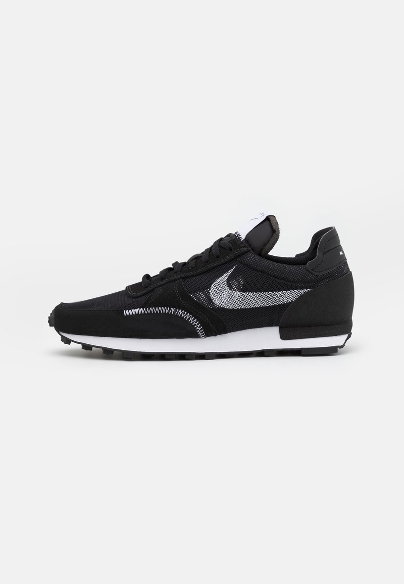 Černé tenisky Nike s bílým logem Swoosh, bílou podrážkou a černým vzorkem, zobrazené z boku na jednoduchém bílém pozadí.
