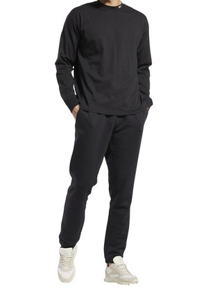 Chemise noire à manches longues avec col rond, assortie à un pantalon de survêtement noir. Portée avec des baskets claires, dotées d'une semelle texturée.