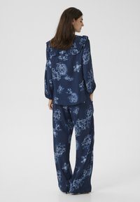 Marinblå blommönstrad outfit med blus med volangkrage och vida byxor, tillverkad av lättviktsmaterial med en texturerad yta.