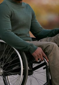 Grön tröja med ribbade muddar, bärs av en person i en manuell rullstol. Rullstolen har stora, silverfärgade ekrar och en svart ram.