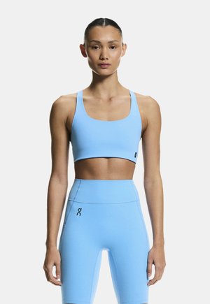 Woman wearing light blue sports bra and high-waisted biker shorts, standing straight against white background.