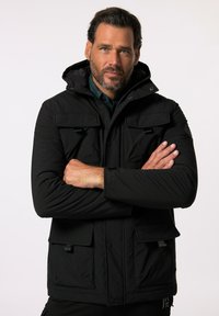 Schwarze gepolsterte Jacke mit Kapuze, verfügt über zwei Fronttaschen und einen Reißverschluss. Strukturierter Stoff mit glatter Oberfläche. Mit Druckknöpfen akzentuiert.