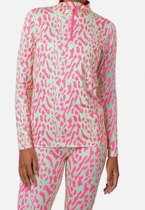 Kobieta ubrana w dopasowany, miętowo-zielony i jaskrawo różowy top z długim rękawem w abstrakcyjny wzór oraz legginsy, top z przodu zapinany na zamek.