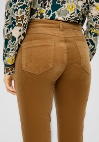 Bruine corduroy broek met een getailleerd ontwerp, voorzien van twee achterzakken en een soepele textuur, gecombineerd met een gebloemd overhemd met lange mouwen.