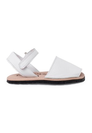 Bílé kožené sandály se zavřenou špičkou, kotníkovým popruhem a plochou černou gumovou podrážkou. Design se vyznačuje čistými liniemi a minimalistickými akcenty.
