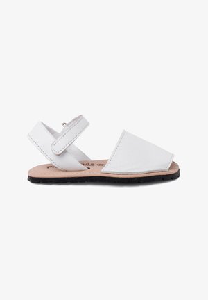 Sandalias de cuero blanco con puntera cerrada, correa en el tobillo y suela plana de goma negra. El diseño presenta líneas limpias y acentos minimalistas.