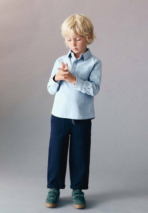 Chemise en denim bleu clair, pantalons larges bleu marine et chaussures vertes. Dotée d'un col boutonné et de manches retroussées. Design simple et décontracté.