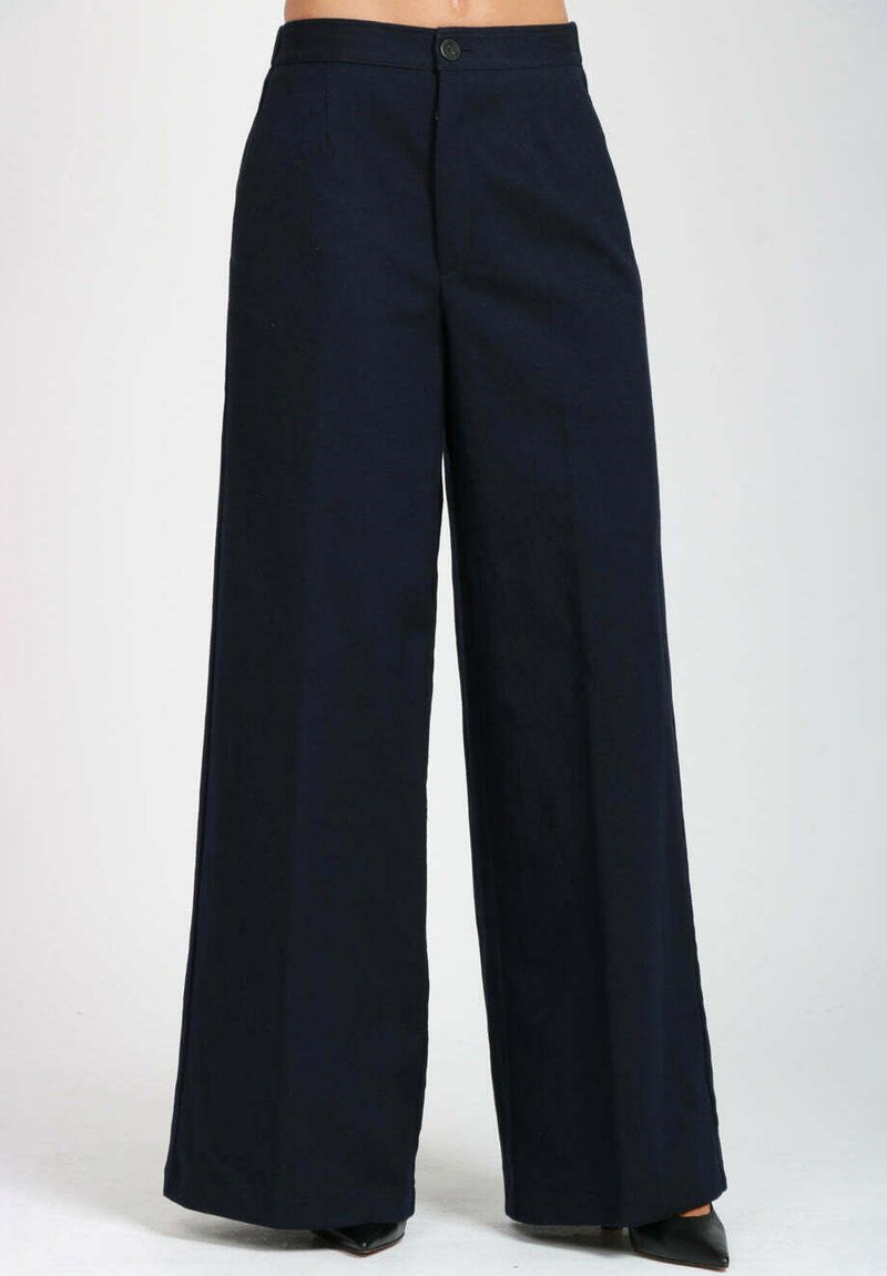 Pantaloni a vita alta ampi di colore blu navy scuro con chiusura frontale a bottone e cerniera, indossati con scarpe nere a punta.