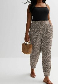 Schwarzes Tanktop, gemusterte, locker sitzende Hose mit einem Zickzackdesign in Beige und Schwarz, Strohtasche und braune Sandalen.