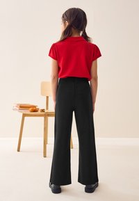 Raudona trumpomis rankovėmis polo marškinėliai su apykakle, derinami su juodomis, plačiomis, aukšto liemens kelnėmis ir juoda avalyne. Paprastas, švarus dizainas.