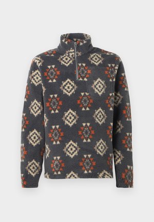 Pull en polaire gris foncé avec un motif géométrique. Présente un col montant, une fermeture éclair à mi-hauteur, et des couleurs d'accent rouge et crème.