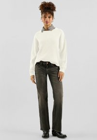 Biały prążkowany sweter noszony na szarej koszuli w kratę, zestawiony z ciemnymi dżinsami o prostych nogawkach i czarnymi botkami za kostkę. Prosty design i tekstury.