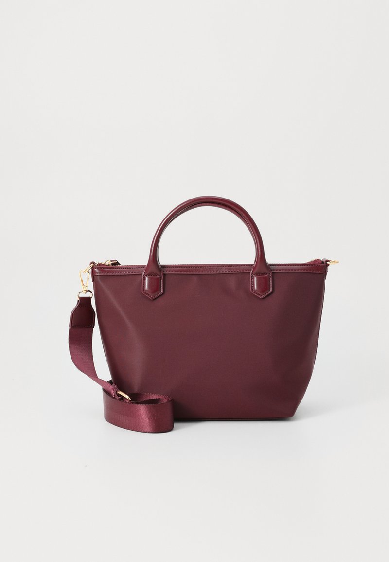 Burgundy tote bag in soft material with two top handles and an adjustable shoulder strap. Features gold-tone hardware and zip closure.