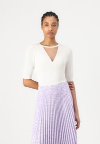 Top crem cu mânecă scurtă, cu o tăietură triunghiulară transparentă, și o fustă plisată lavandă cu un model floral. Textură netedă, corset ajustat.