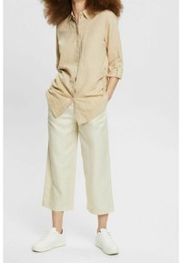 Beige button-up shirt with rolled sleeves, paired with cream wide-leg trousers and white sneakers, showcasing a relaxed fit and lightweight fabric.