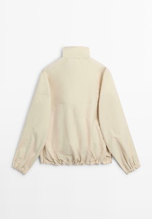 Beige jakke med høj krave, lange ærmer og elastiske manchetter, elastisk kant, vist bagfra på hvid baggrund.