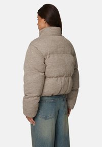 Brązowa kurtka puchowa z wysokim kołnierzem, teksturowana tkanina i elastyczny dół. Noszona z jasnoniebieskimi spodniami typu wide-leg.