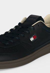 Μαύρο αθλητικό παπούτσι Tommy Jeans με μαύρα κορδόνια, μπεζ εσωτερική επένδυση, σκούρα καφέ σόλα και λογότυπο Tommy στο πλάι και στη γλώσσα.
