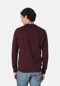 Maglione in maglia di colore bordeaux scuro, con scollo rotondo e maniche lunghe. Dettagli di cuciture visibili e design a vestibilità morbida.