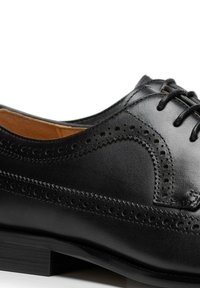 Czarny skórzany but z ażurowymi zdobieniami, gładką fakturą, zaokrąglonym noskiem oraz wiązaniem na sznurówki i niskim, warstwowym obcasem.