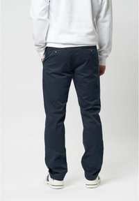 Navy blue puuvillahousut suoran mitoituksen kanssa, joissa on takataskut ja hienovaraiset ommel yksityiskohdat, yhdistettynä valkoisiin tennareihin.
